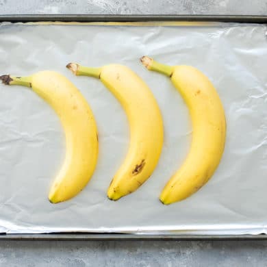 3 unpeeled yellow bananas on a foil-lined baking sheet.