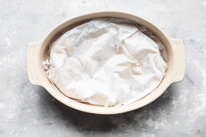 Lemon pepper chicken wrapped in paper in a baking dish.