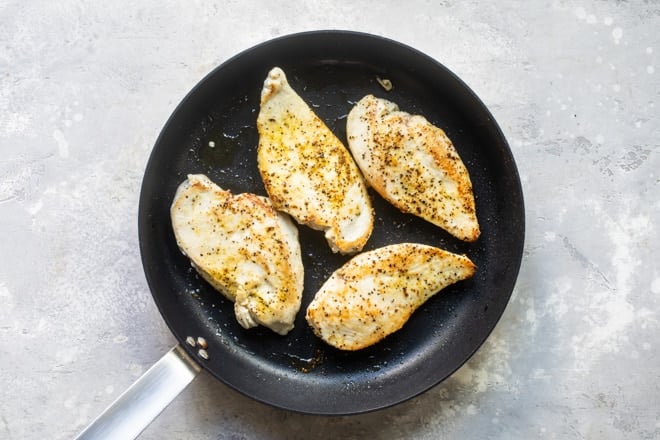 Lemon pepper chicken being seared on a black skillet.