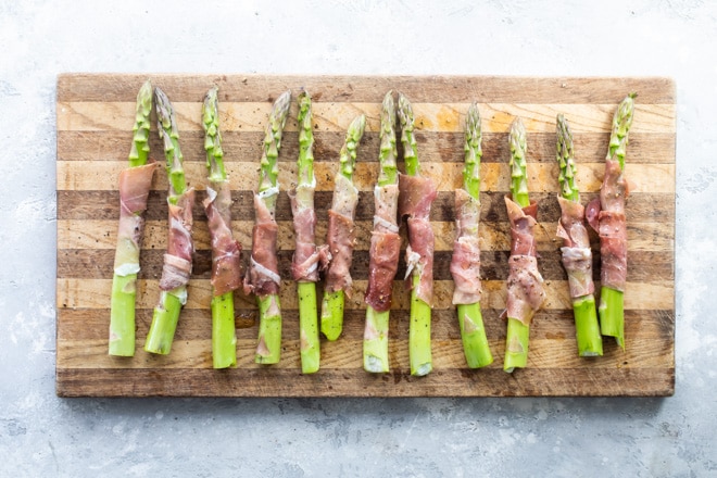 Prosciutto wrapped asparagus on a cutting board.