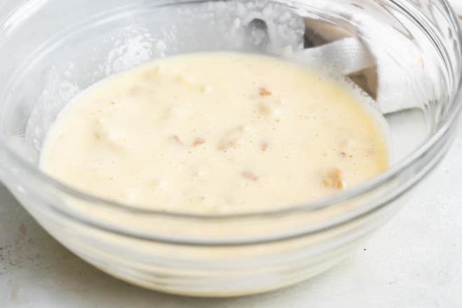 Bread, cream and egg mixture in a clear bowl.