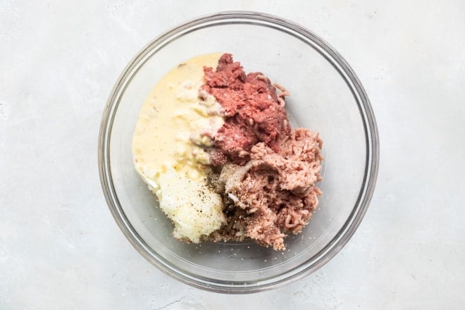 Meatball ingredients being combined in a glass bowl.