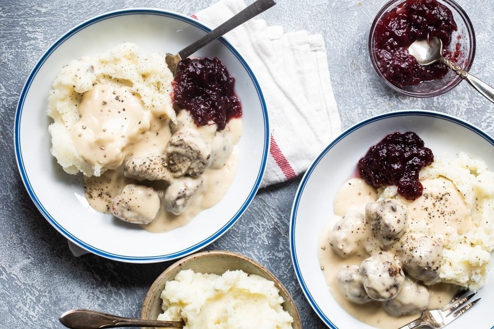 Swedish meatballs on plates with mashed potatoes, gravy, and cranberry sauce.