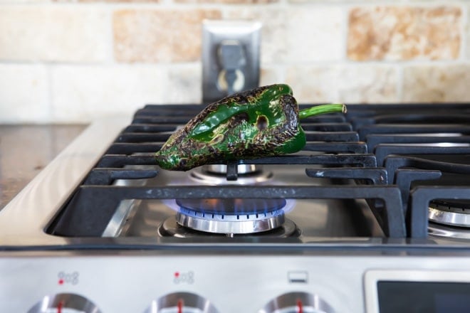 Poblano pepper being roasted on top of a stove.