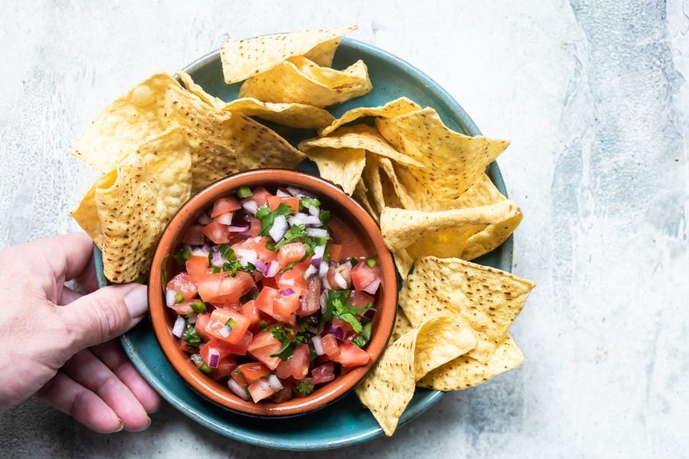 Chipotle tomato salsa in a black bowl on a blue plate with tortilla chips.