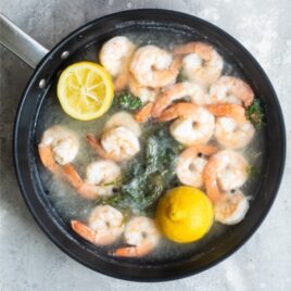 Shrimp being poached in boiling water with lemon halves in a black skillet.