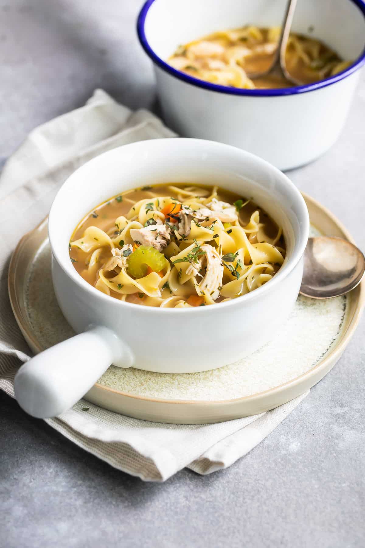 Chicken noodle soup in a white handled bowl.