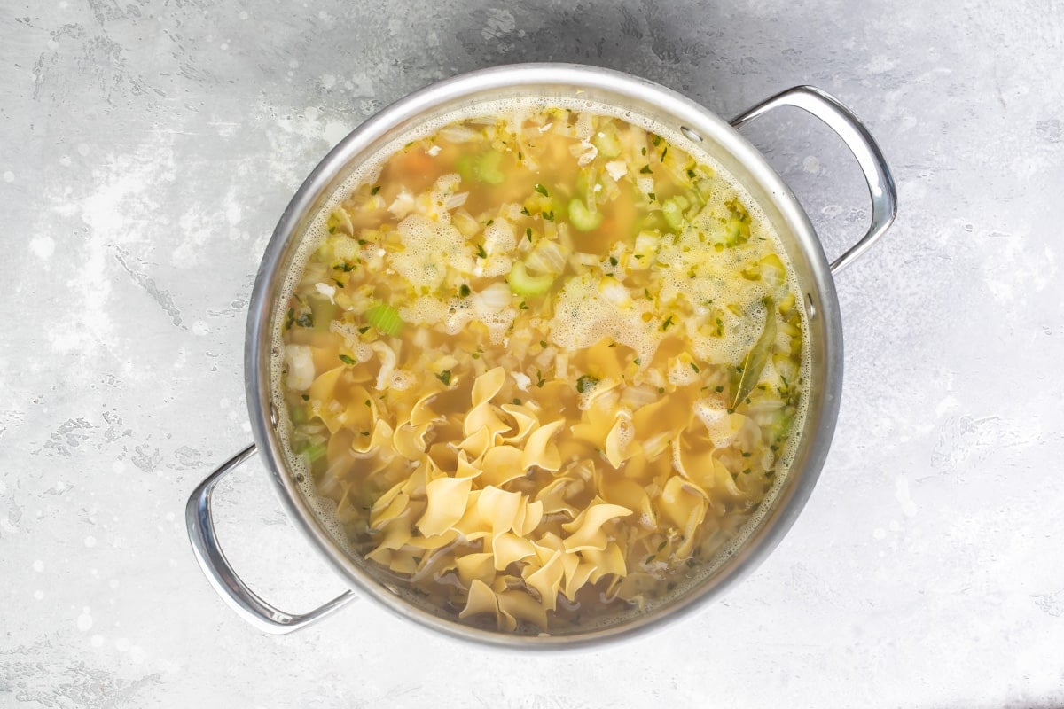 Chicken noodle soup cooking in a silver pot.