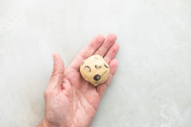 A hand holding a ball of chocolate chip cookie dough.