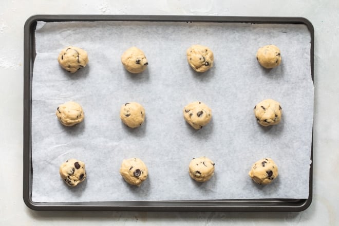 Balls of frozen cookie dough on a baking sheet before going in the oven.