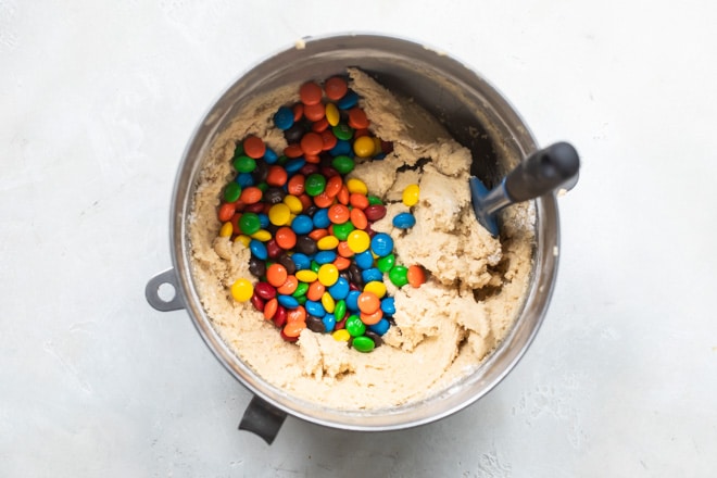 A mixing bowl with cookie dough and M&Ms sitting on it.