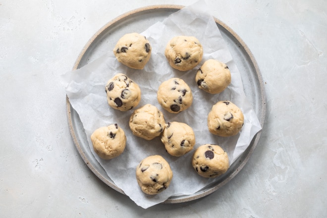 Balls of cookie dough on a round tray lined with parchment paper.