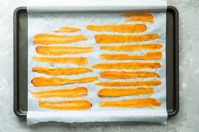 Long carrot peels on a piece of parchment paper on a sheet pan.
