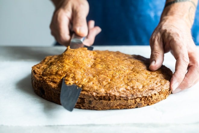 Someone slicing off a fine layer of cake from a layer of carrot cake.