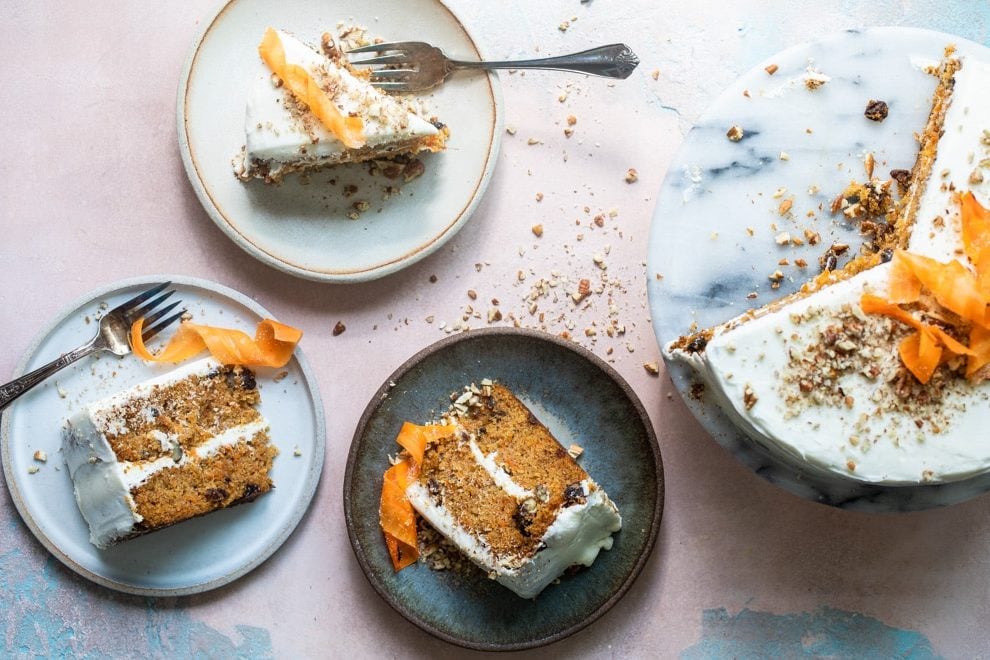 Three slices of carrot cake on plates with forks and the cake on a black and white marble platter.