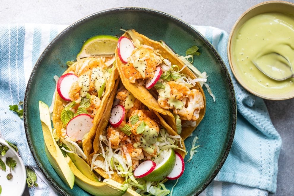 Cauliflower Tinga tacos on a blue plate with a side of avocado sauce.