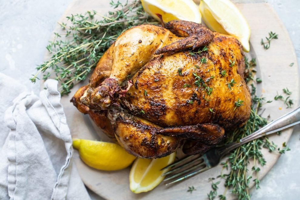A rotisserie chicken on a white plate with slices of lemon.