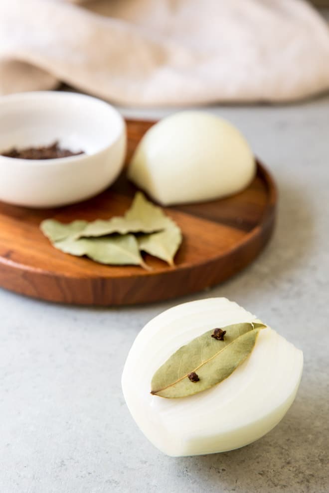 Half of an onion with a bay leaf attached to it with whole cloves.