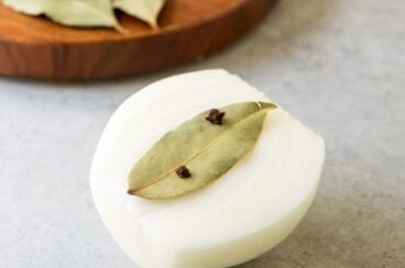 Half of an onion with a bay leaf attached to it with whole cloves.