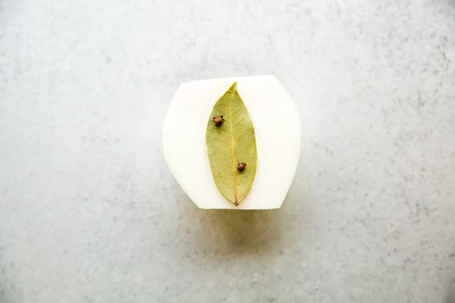 Half of an onion with a bay leaf attached to it with whole cloves.