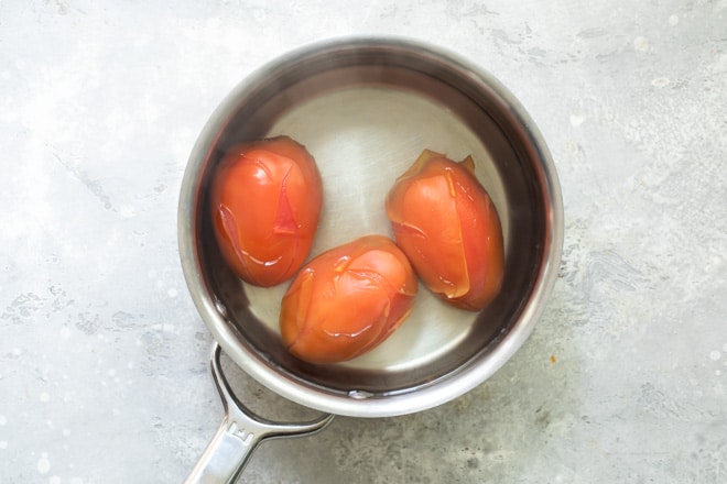Three tomatoes in boiling water in a silver pot.