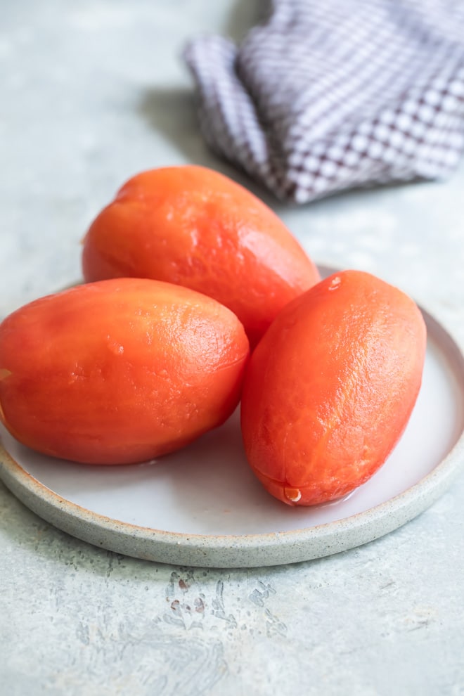 Three peeled tomatoes on a white plate.