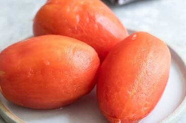 Three peeled tomatoes on a white plate.