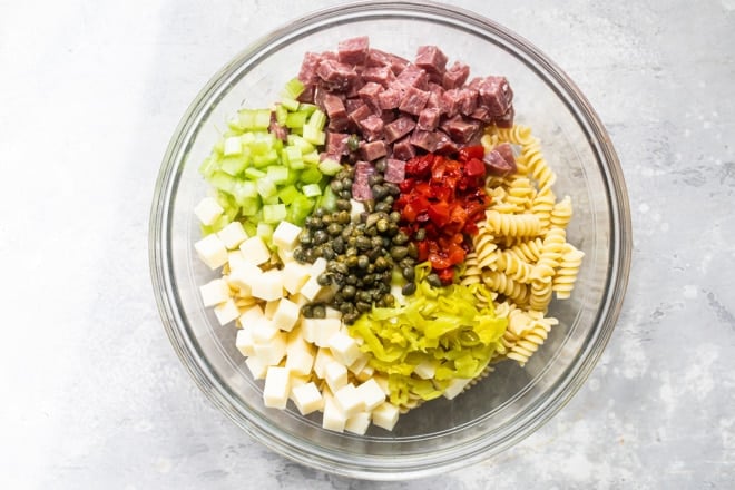 Separated Italian pasta salad ingredients in a clear bowl.