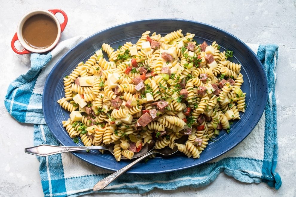 Italian pasta salad on a blue platter with a serving spoon and fork.