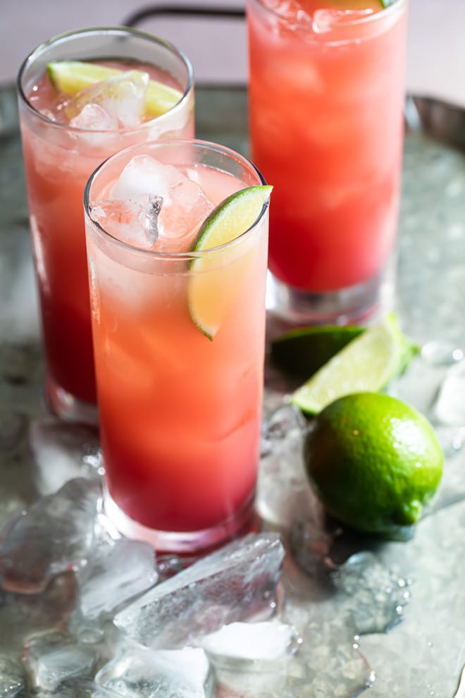 Seabreeze cocktail in three glasses on a silver serving tray with ice and sliced and whole limes.