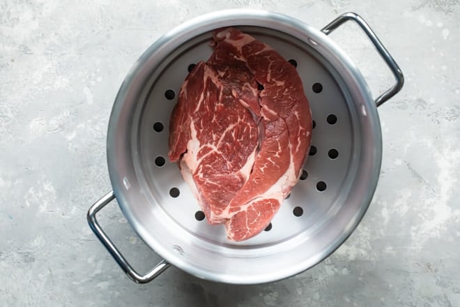 Beef in a silver steamer basket inside a pot.
