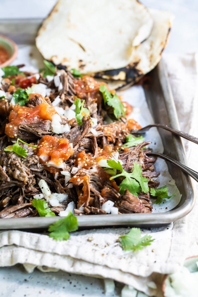 Garnished birria on a silver baking sheet.