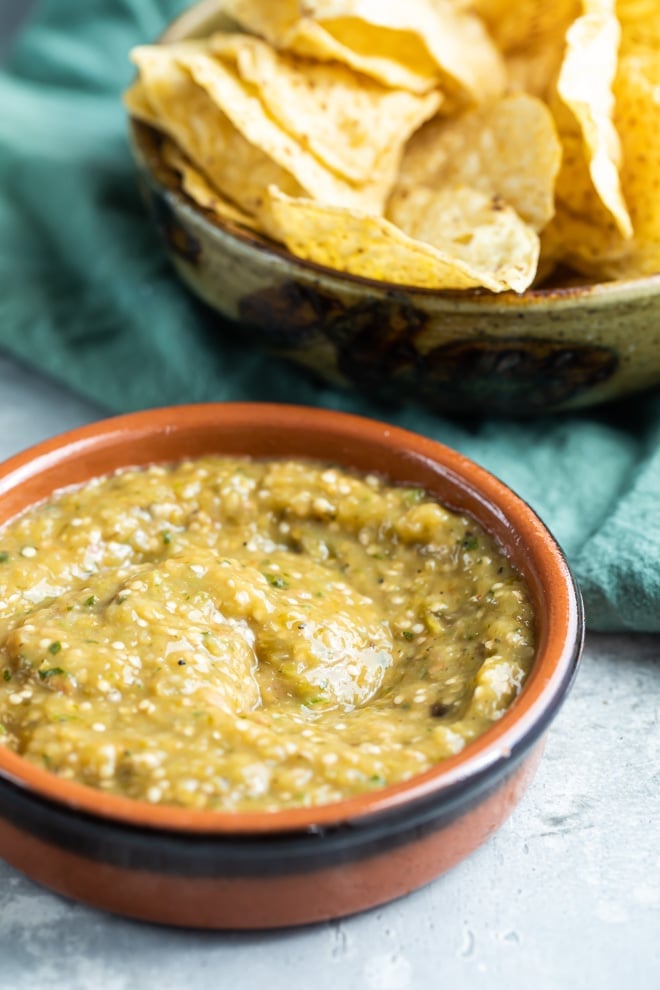 Chipotle tomatillo green chili salsa in a red bowl and a bowl of chips.