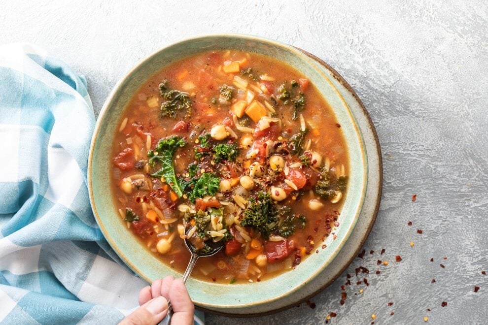 Minestrone soup in a white bowl with a sliver spoon.