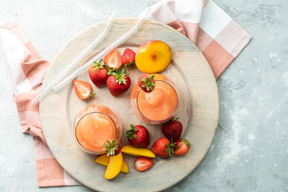 Two glasses of strawberry peach frose on a plate surrounded by slices of strawberries and peaches.