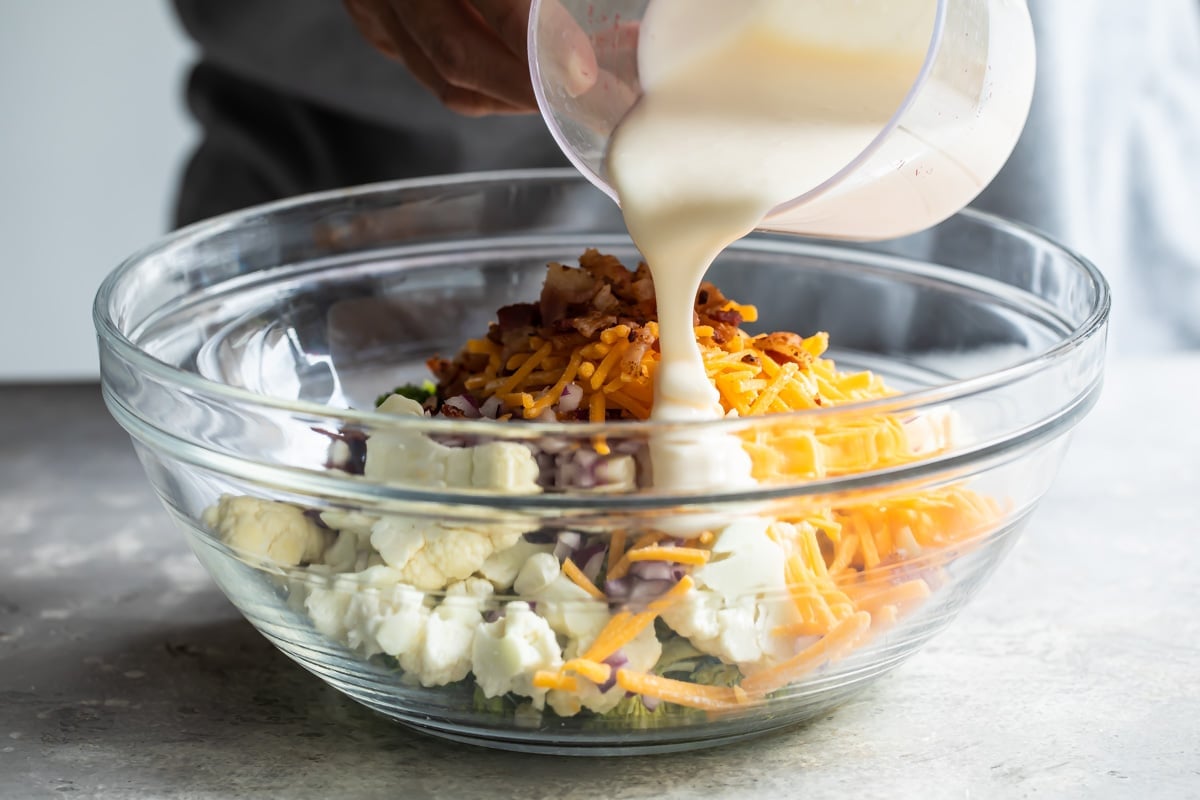 Dressing being poured onto a broccoli salad.