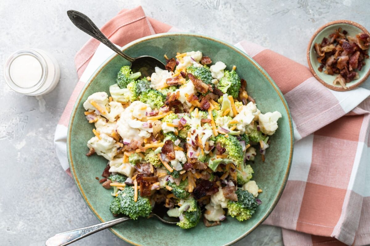 Broccoli salad with bacon and cheese in a bowl with two serving spoons in it.