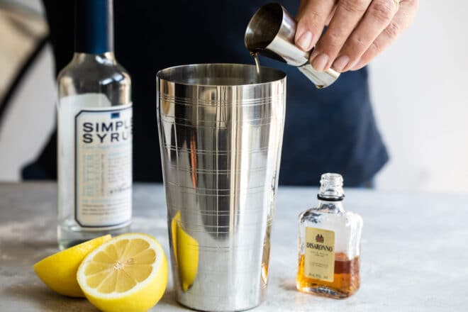 Amaretto sour ingredients being added to a martini shaker.