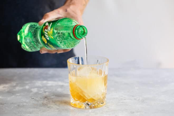 Lemon-lime soda being poured over an amaretto sour.