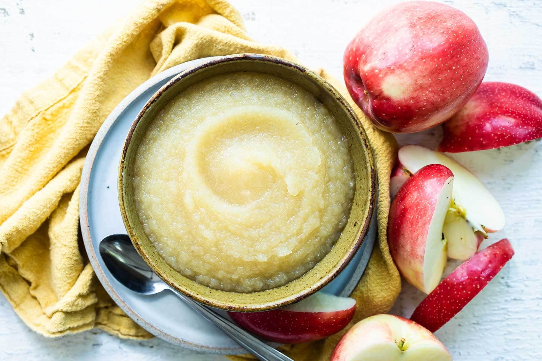 Applesauce in a light green bowl with apples in the background.