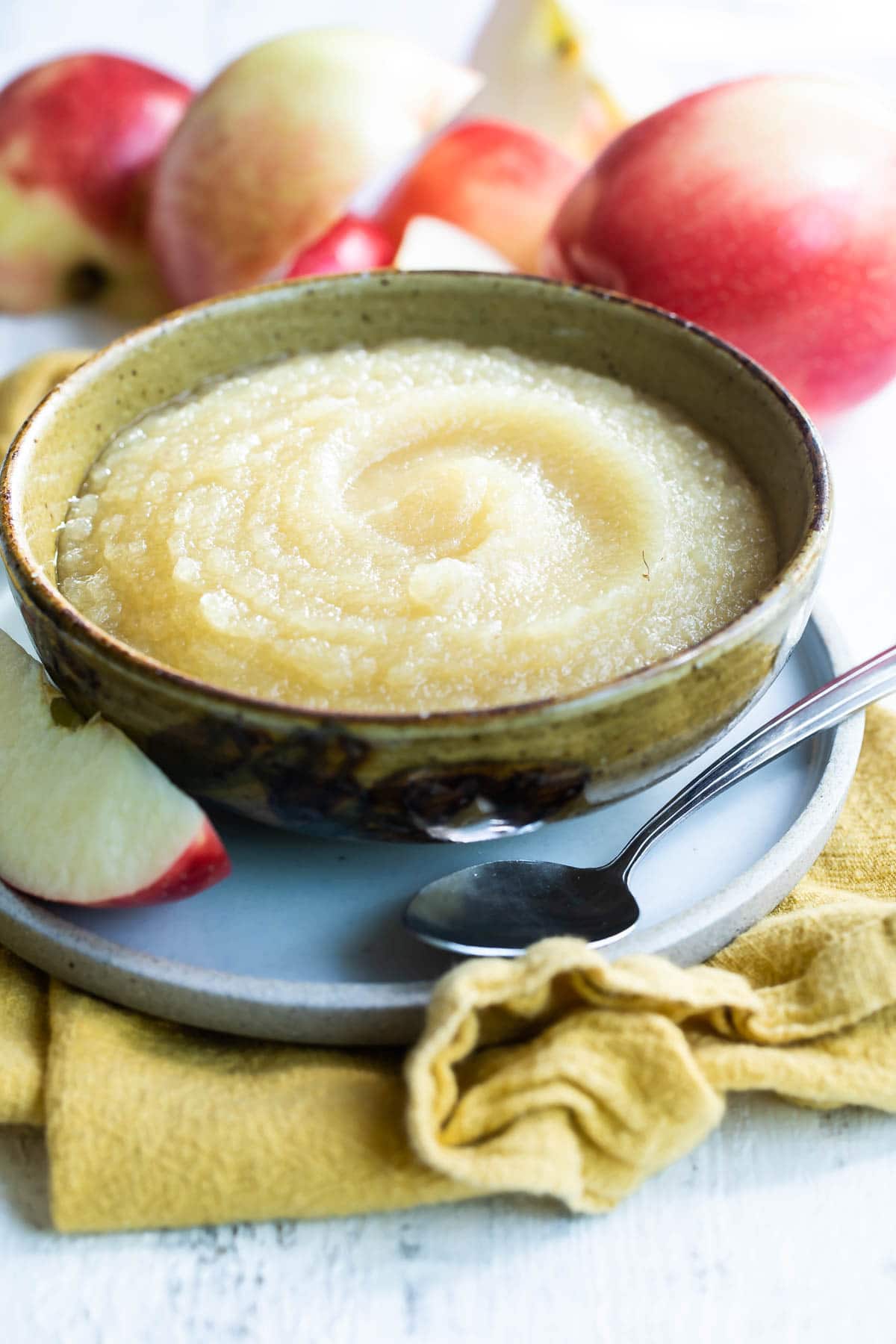 Applesauce in a light green bowl with apples in the background.