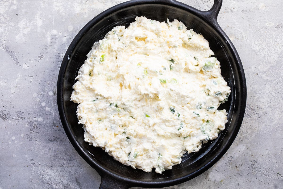 Uncooked cheesy bacon dip in a cast iron skillet.