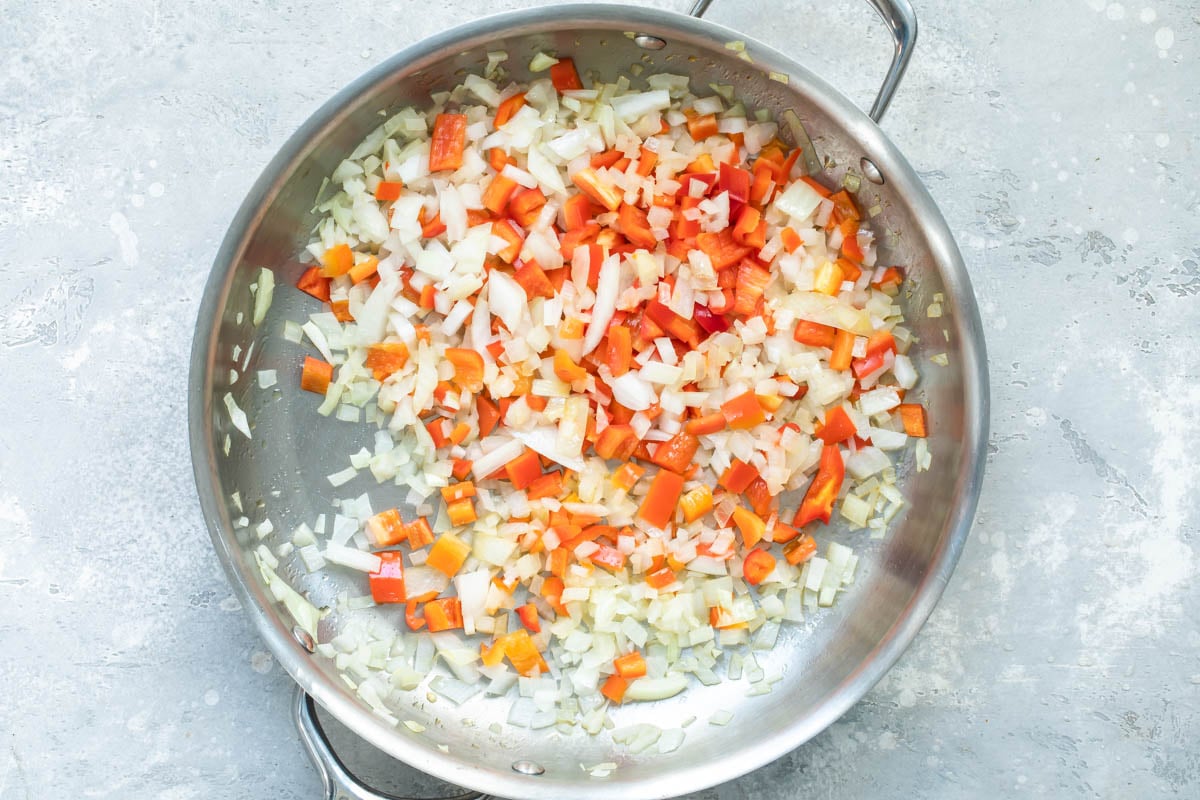 Various vegetables being cooked in a silver skillet.