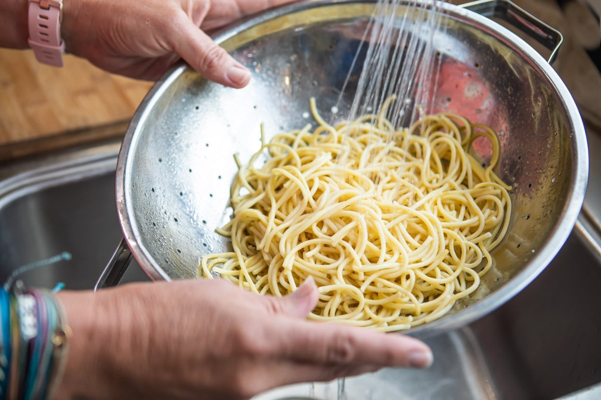 Spaghetti noodles being rinsed in a colander.