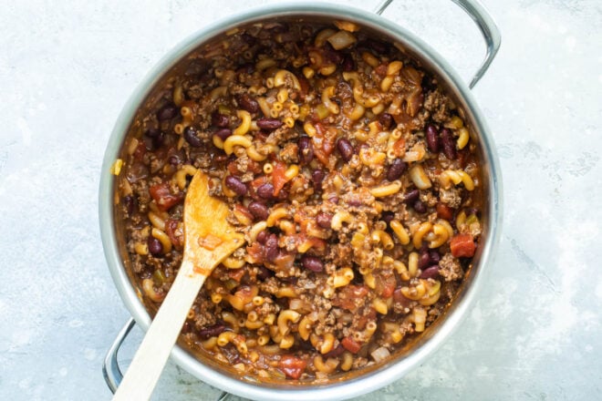 Chili mac in a Dutch oven with a wooden spoon resting in it.