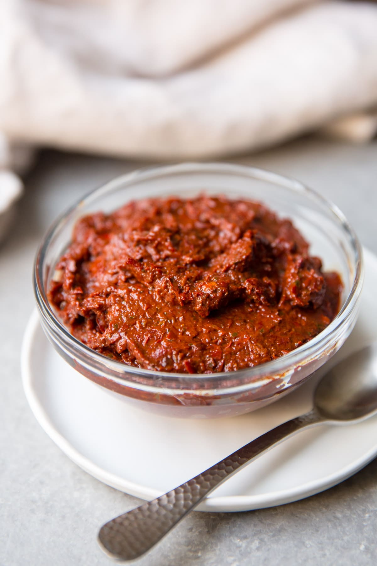 A bowl of harissa paste on a plate with a spoon next to it.