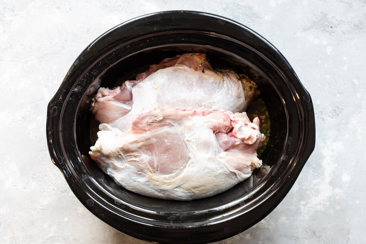 A turkey breast in a black slow cooker.