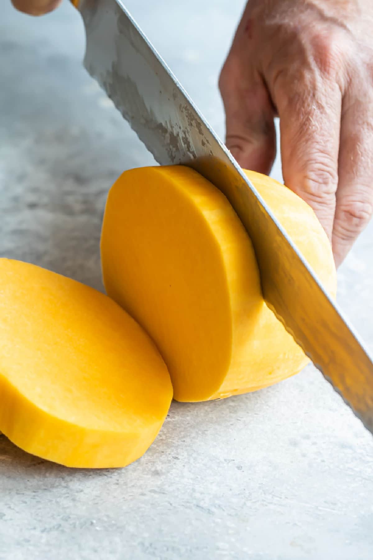 Peeled butternut squash being sliced into rounds.