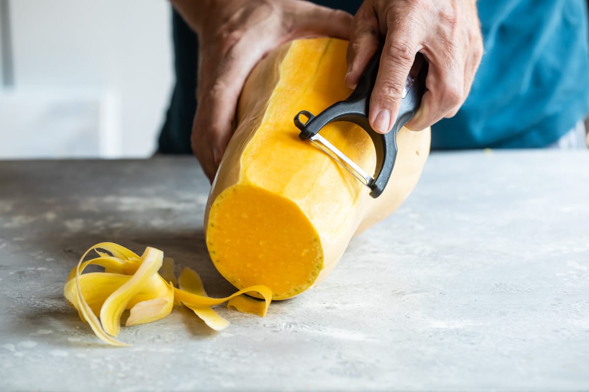 Peeling butternut squash with a vegetable peeler.