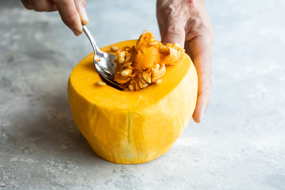 Scooping seeds out of half a peeled butternut squash.